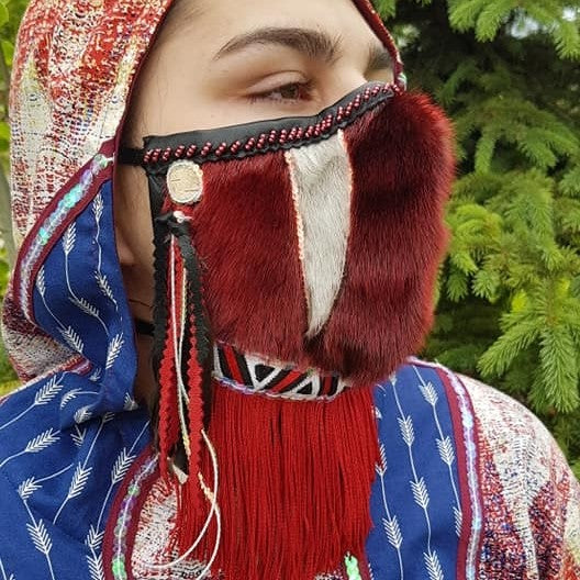 Taalrumiq, Inuvialuit Fortitude, 2021.  Pandemic mask made of red sealskin with fringe, geometric trim, beads, sequins, birch bark, ptarmigan feather.